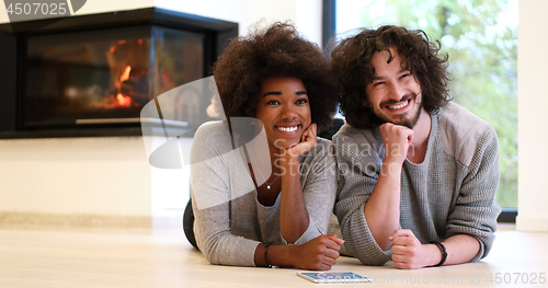 Image of multiethnic couple lying on the floor  in front of fireplace