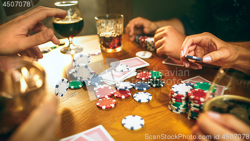 Image of Side view photo of friends sitting at wooden table. Friends having fun while playing board game.