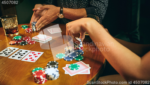 Image of Side view photo of friends sitting at wooden table. Friends having fun while playing board game.