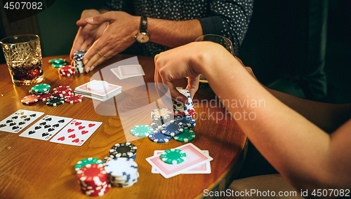 Image of Side view photo of friends sitting at wooden table. Friends having fun while playing board game.