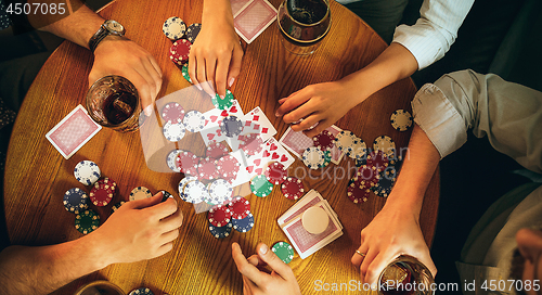 Image of Top view photo of friends sitting at wooden table. Friends having fun while playing board game.