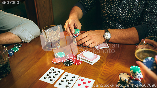 Image of Side view photo of friends sitting at wooden table. Friends having fun while playing board game.