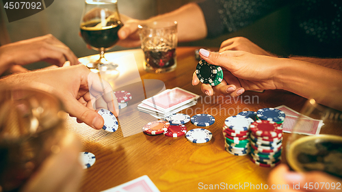 Image of Side view photo of friends sitting at wooden table. Friends having fun while playing board game.