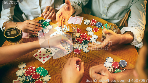 Image of Side view photo of friends sitting at wooden table. Friends having fun while playing board game.