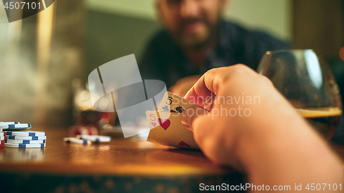 Image of Side view photo of friends sitting at wooden table. Friends having fun while playing board game.