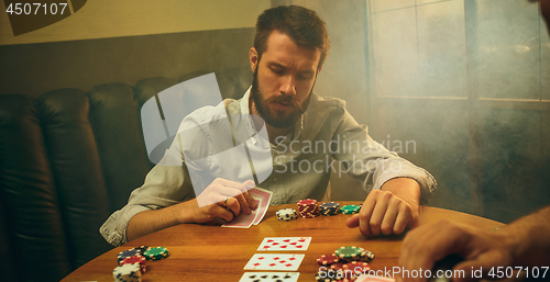 Image of Side view photo of friends sitting at wooden table. Friends having fun while playing board game.