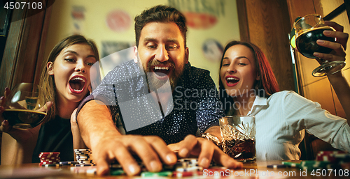 Image of Side view photo of friends sitting at wooden table. Friends having fun while playing board game.