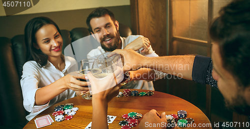 Image of Side view photo of friends sitting at wooden table. Friends having fun while playing board game.