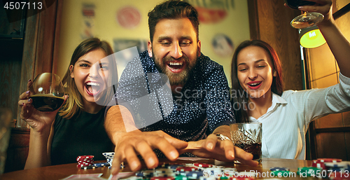 Image of Side view photo of friends sitting at wooden table. Friends having fun while playing board game.