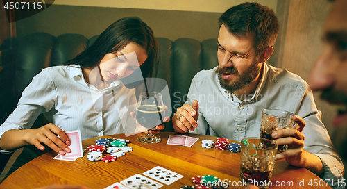 Image of Side view photo of friends sitting at wooden table. Friends having fun while playing board game.