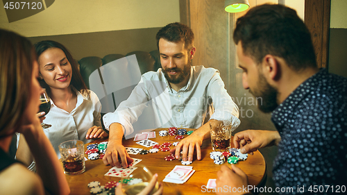 Image of Side view photo of friends sitting at wooden table. Friends having fun while playing board game.