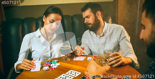 Image of Side view photo of friends sitting at wooden table. Friends having fun while playing board game.