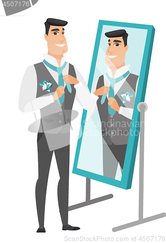 Image of Groom looking in the mirror and adjusting tie.