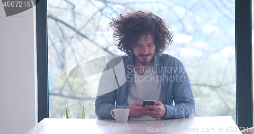 Image of young man drinking coffee and using a mobile phone  at home