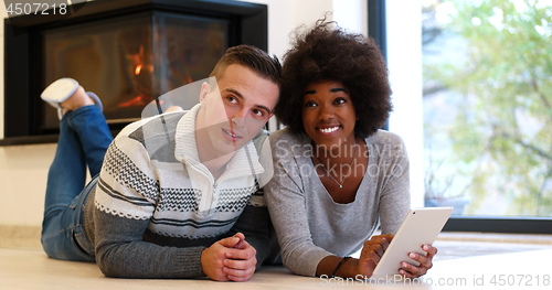 Image of multiethnic couple using tablet computer on the floor