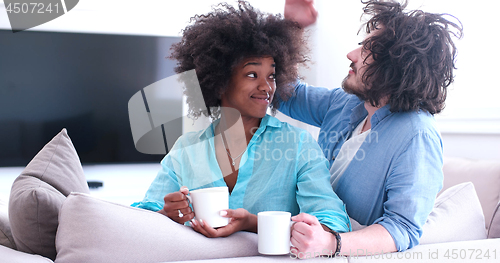 Image of multiethnic couple sitting on sofa at home drinking coffe