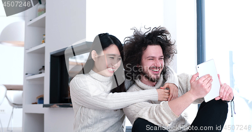 Image of young multiethnic couple using a tablet on the floor