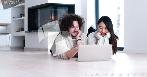 Image of young multiethnic couple using a laptop on the floor