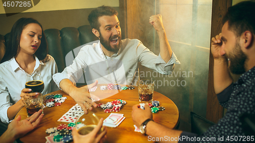 Image of Side view photo of friends sitting at wooden table. Friends having fun while playing board game.