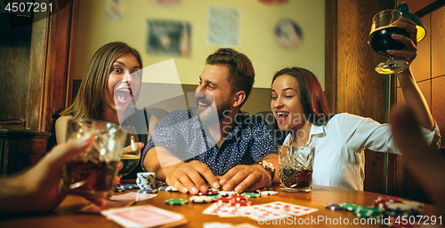 Image of Side view photo of friends sitting at wooden table. Friends having fun while playing board game.