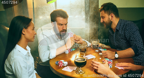 Image of Side view photo of friends sitting at wooden table. Friends having fun while playing board game.