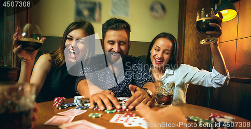 Image of Side view photo of friends sitting at wooden table. Friends having fun while playing board game.