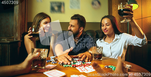 Image of Side view photo of friends sitting at wooden table. Friends having fun while playing board game.