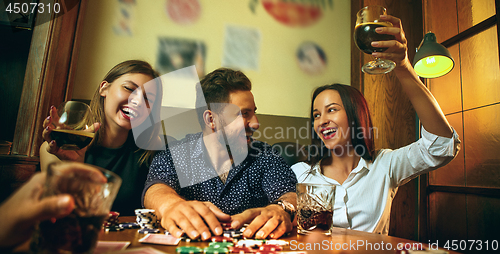 Image of Side view photo of friends sitting at wooden table. Friends having fun while playing board game.