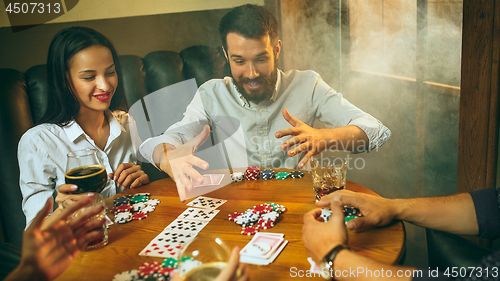 Image of Side view photo of friends sitting at wooden table. Friends having fun while playing board game.
