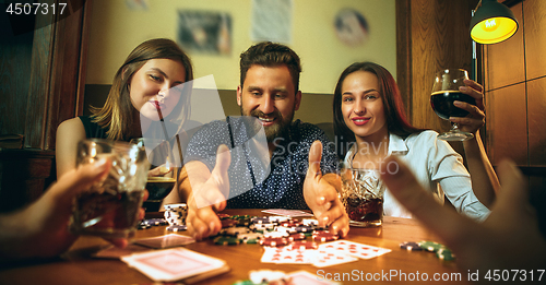 Image of Side view photo of friends sitting at wooden table. Friends having fun while playing board game.