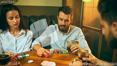 Image of Side view photo of friends sitting at wooden table. Friends having fun while playing board game.