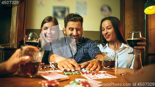 Image of Side view photo of friends sitting at wooden table. Friends having fun while playing board game.