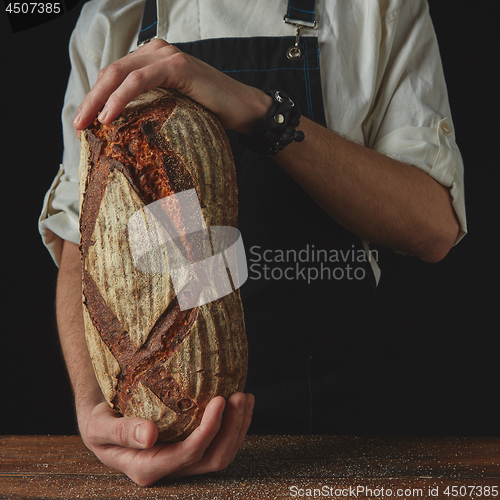 Image of Baker\'s hands hold an oval bread.