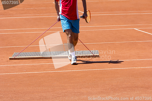 Image of Player aligns surface tennis court, with pulling network