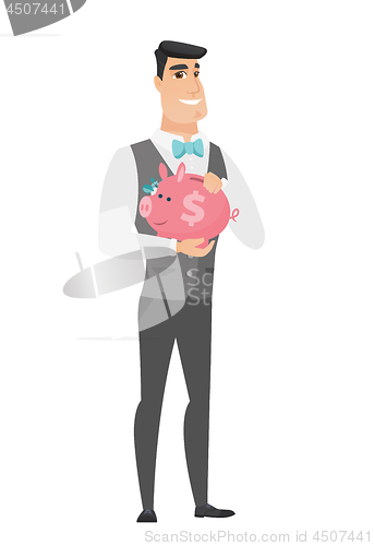 Image of Caucasian groom holding a piggy bank.