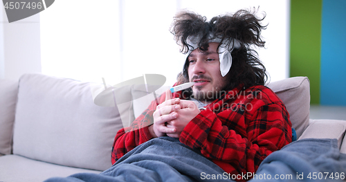 Image of sick man is holding a cup while sitting on couch