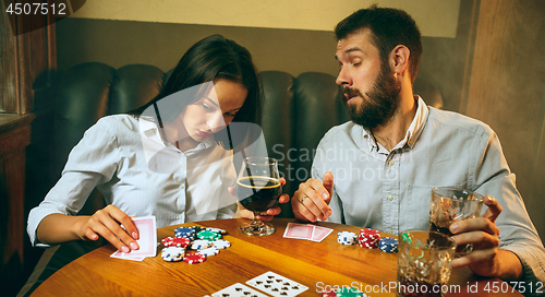 Image of Side view photo of friends sitting at wooden table. Friends having fun while playing board game.