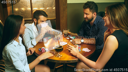 Image of Side view photo of friends sitting at wooden table. Friends having fun while playing board game.