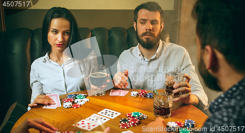 Image of Side view photo of friends sitting at wooden table. Friends having fun while playing board game.