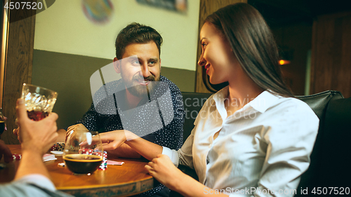 Image of Side view photo of friends sitting at wooden table. Friends having fun while playing board game.