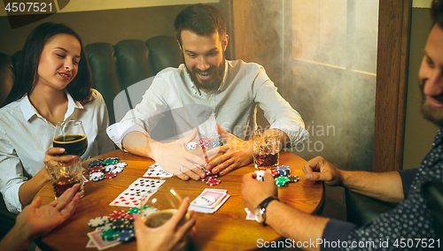 Image of Side view photo of friends sitting at wooden table. Friends having fun while playing board game.