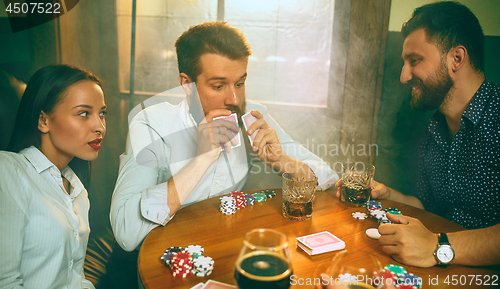 Image of Side view photo of friends sitting at wooden table. Friends having fun while playing board game.