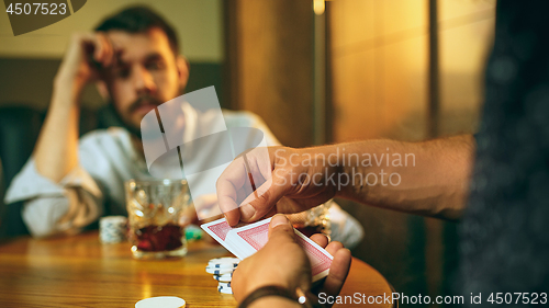 Image of Side view photo of friends sitting at wooden table. Friends having fun while playing board game.