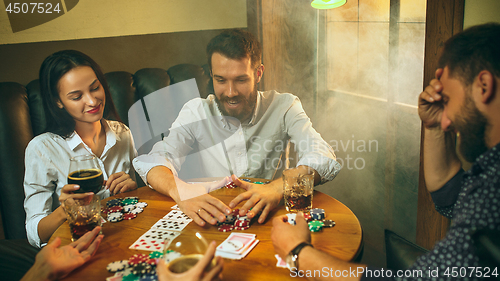 Image of Side view photo of friends sitting at wooden table. Friends having fun while playing board game.