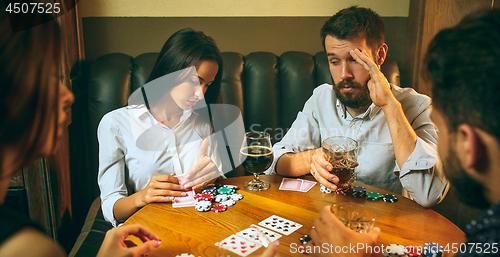 Image of Side view photo of friends sitting at wooden table. Friends having fun while playing board game.