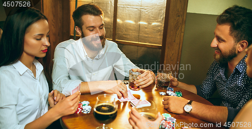 Image of Side view photo of friends sitting at wooden table. Friends having fun while playing board game.