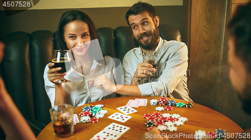 Image of Side view photo of friends sitting at wooden table. Friends having fun while playing board game.