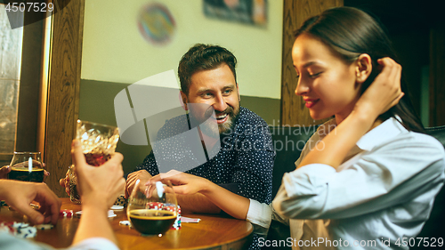 Image of Side view photo of friends sitting at wooden table. Friends having fun while playing board game.