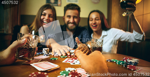 Image of Side view photo of friends sitting at wooden table. Friends having fun while playing board game.