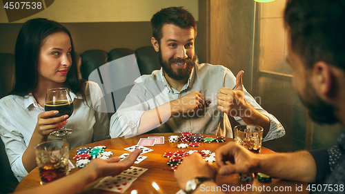 Image of Side view photo of friends sitting at wooden table. Friends having fun while playing board game.